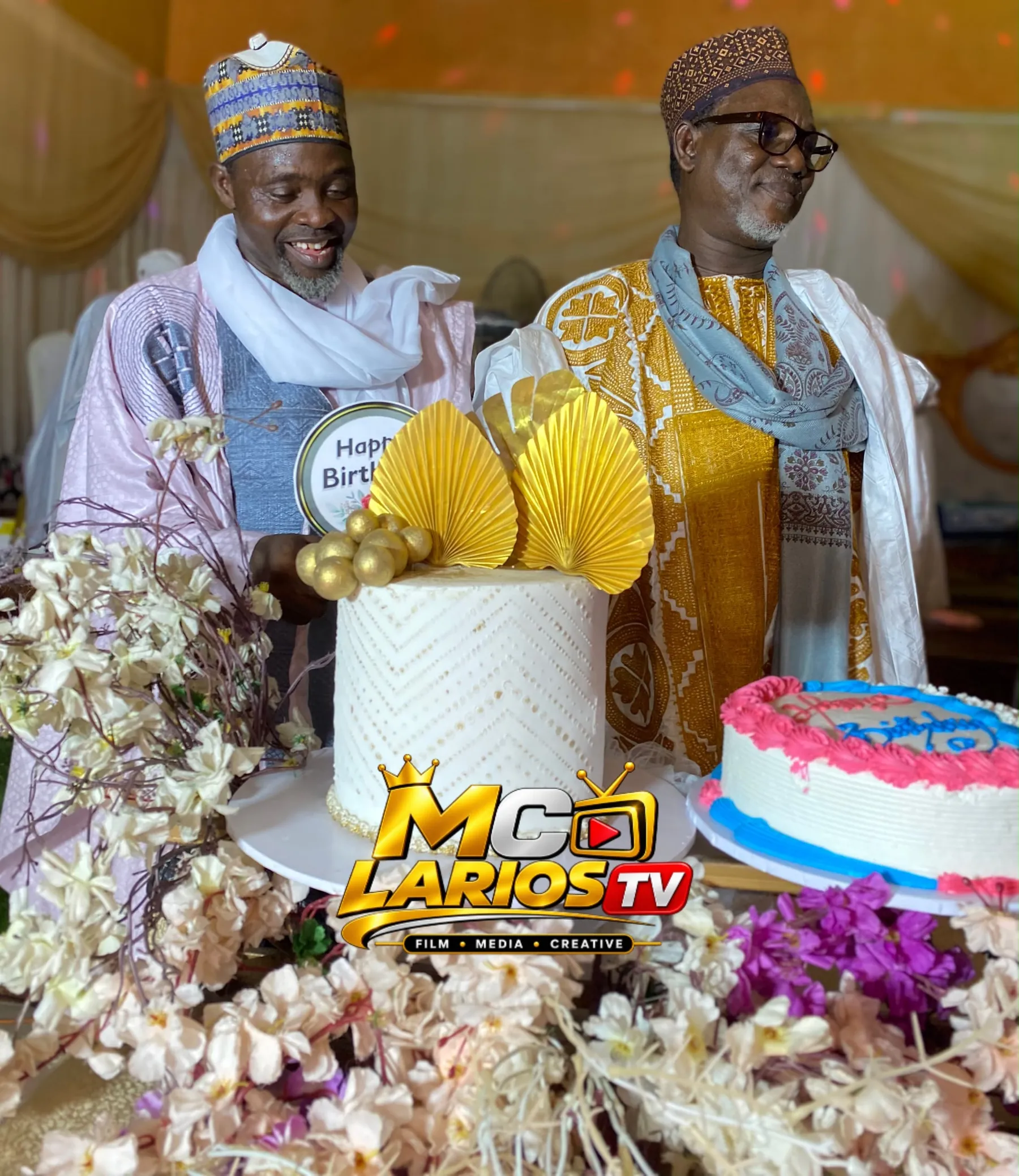 Two elders smiling beside a white and gold cake decorated with gold fans