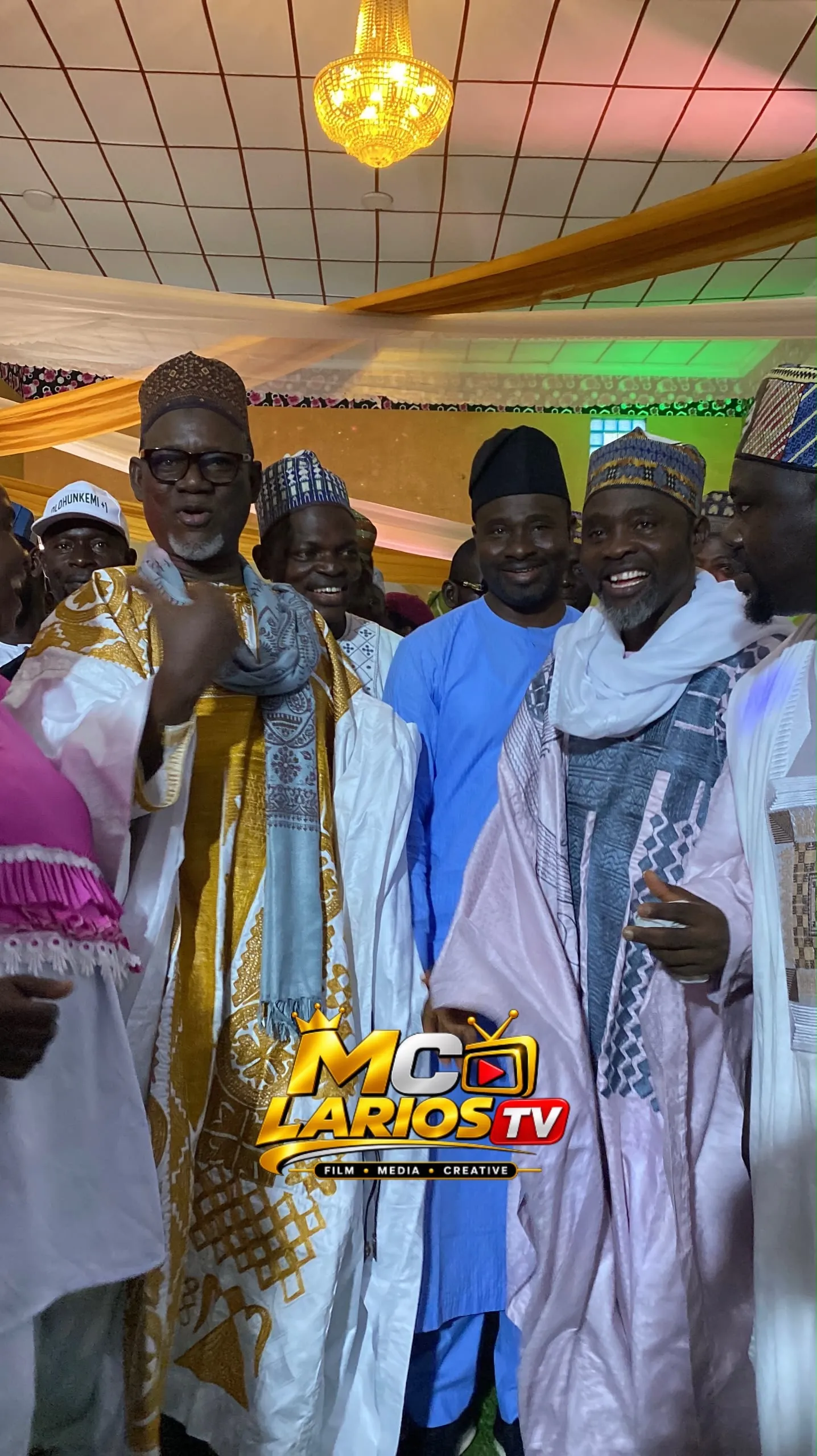 A group of men in embroidered robes and caps standing together under a chandelier