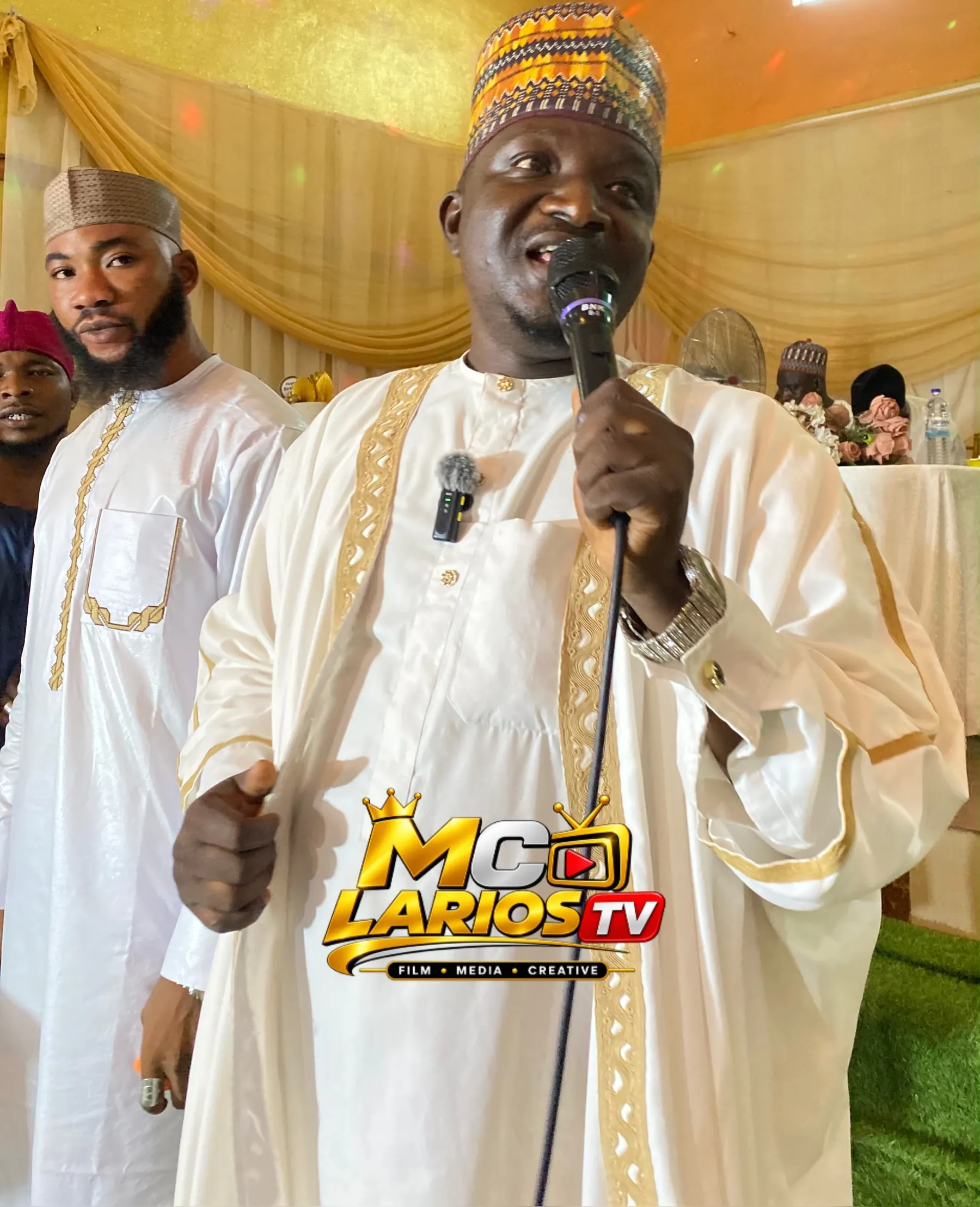 A man in a cream robe with gold trim speaking into a microphone