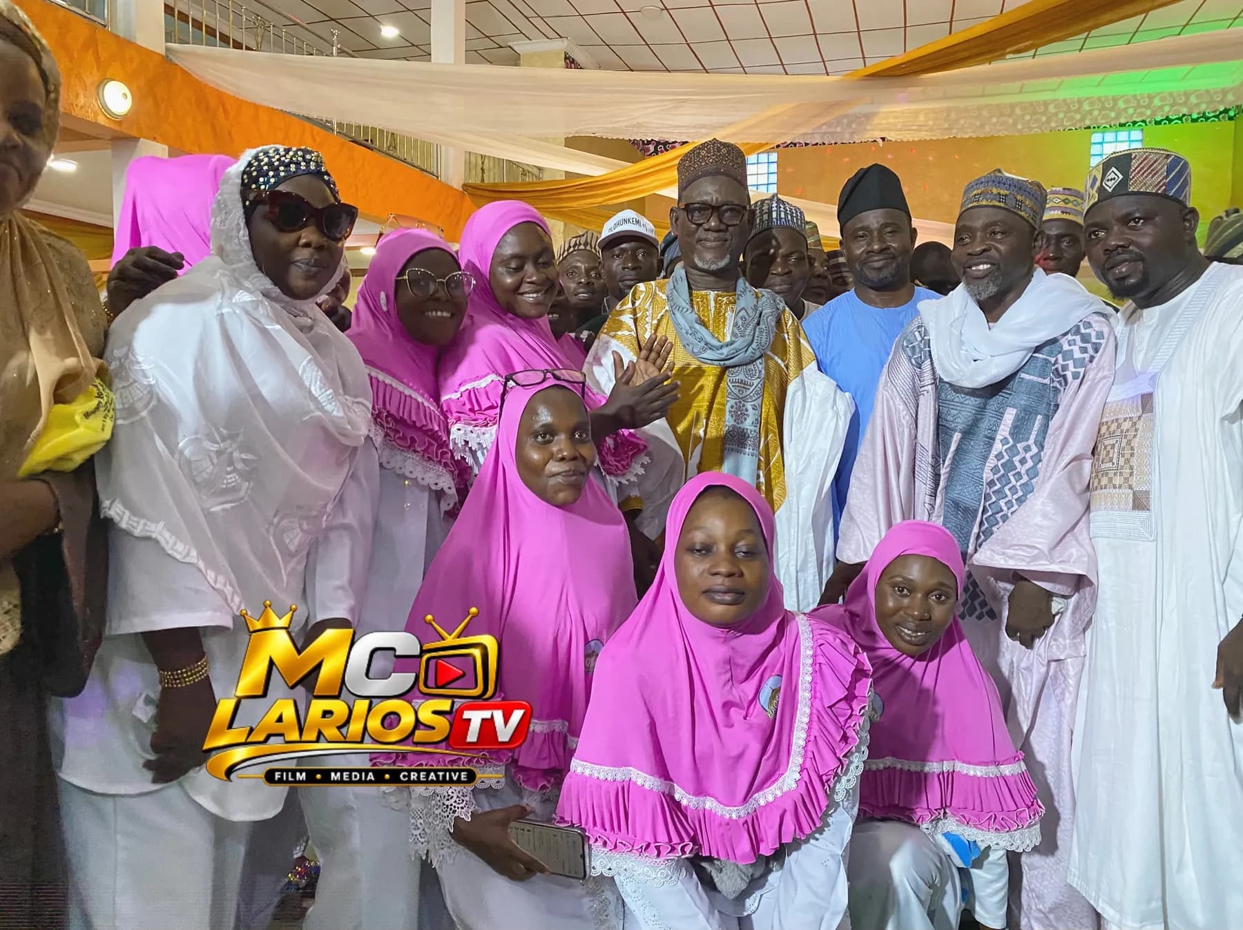 Women in pink hijabs and men in embroidered robes gathered for a group photograph