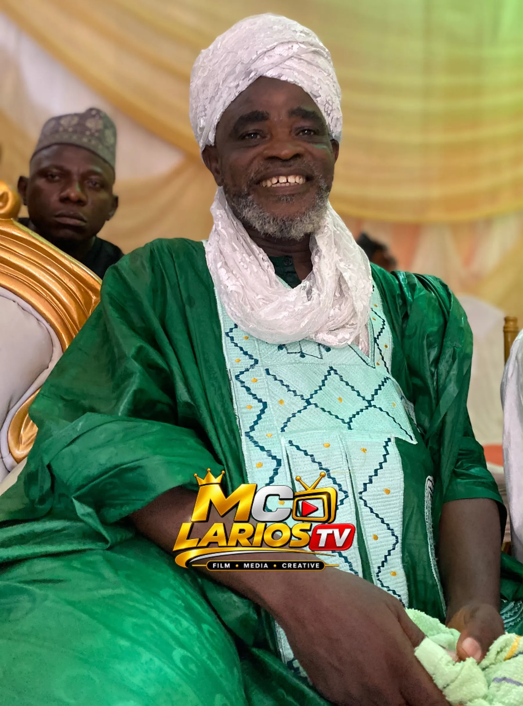 A smiling elder in a green robe and white lace turban