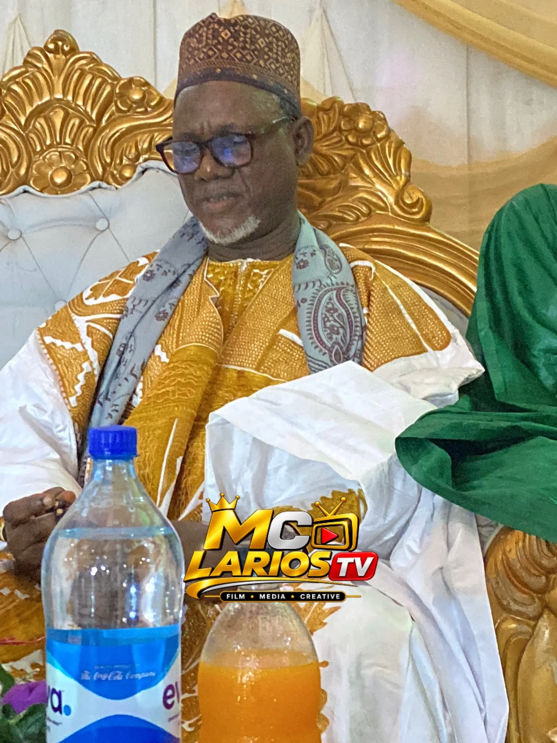 A dignitary in white and gold seated on an ornate chair