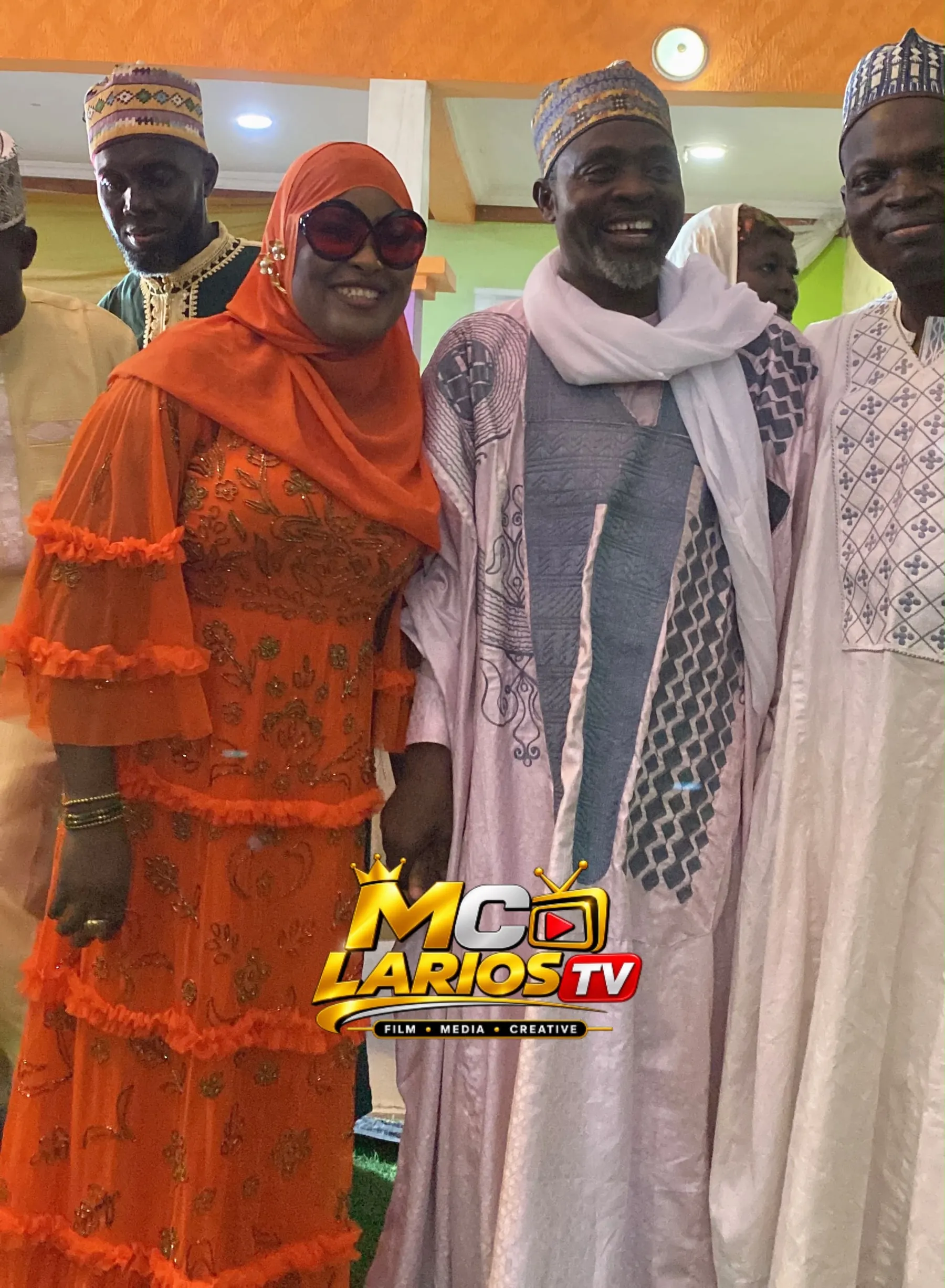 A woman in an orange dress and hijab with men in embroidered robes