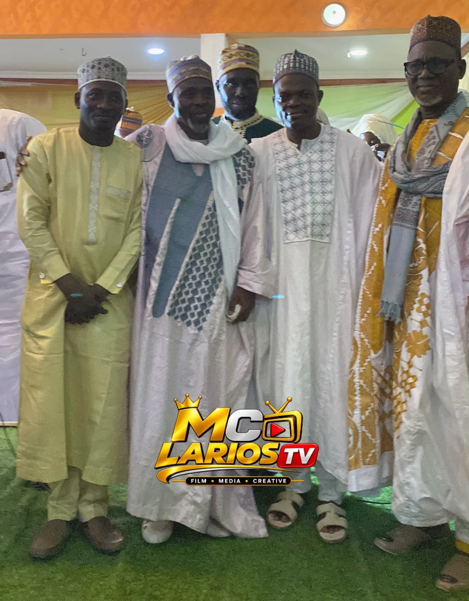 Five men in embroidered robes and caps standing together on green carpet
