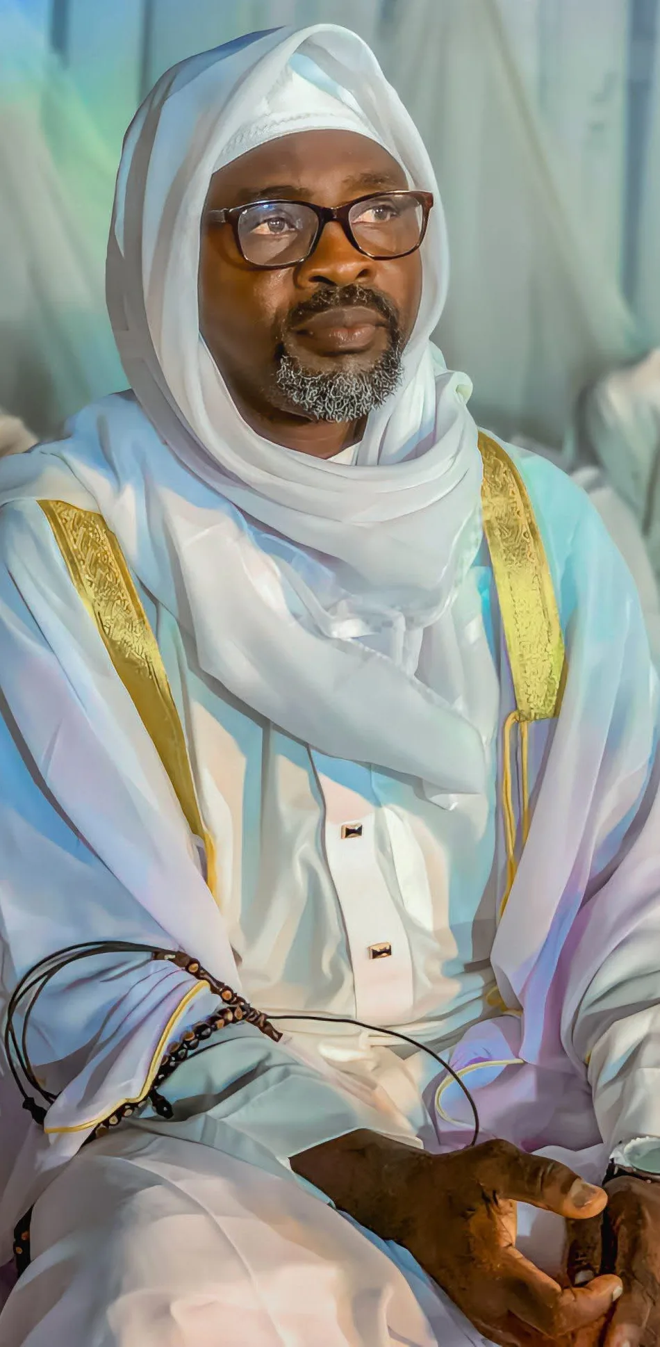 Sheikh AbdulGaniyy Olohunkemi Abiodun, seated, wearing a white robe with gold embroidered trim and a white head wrap
